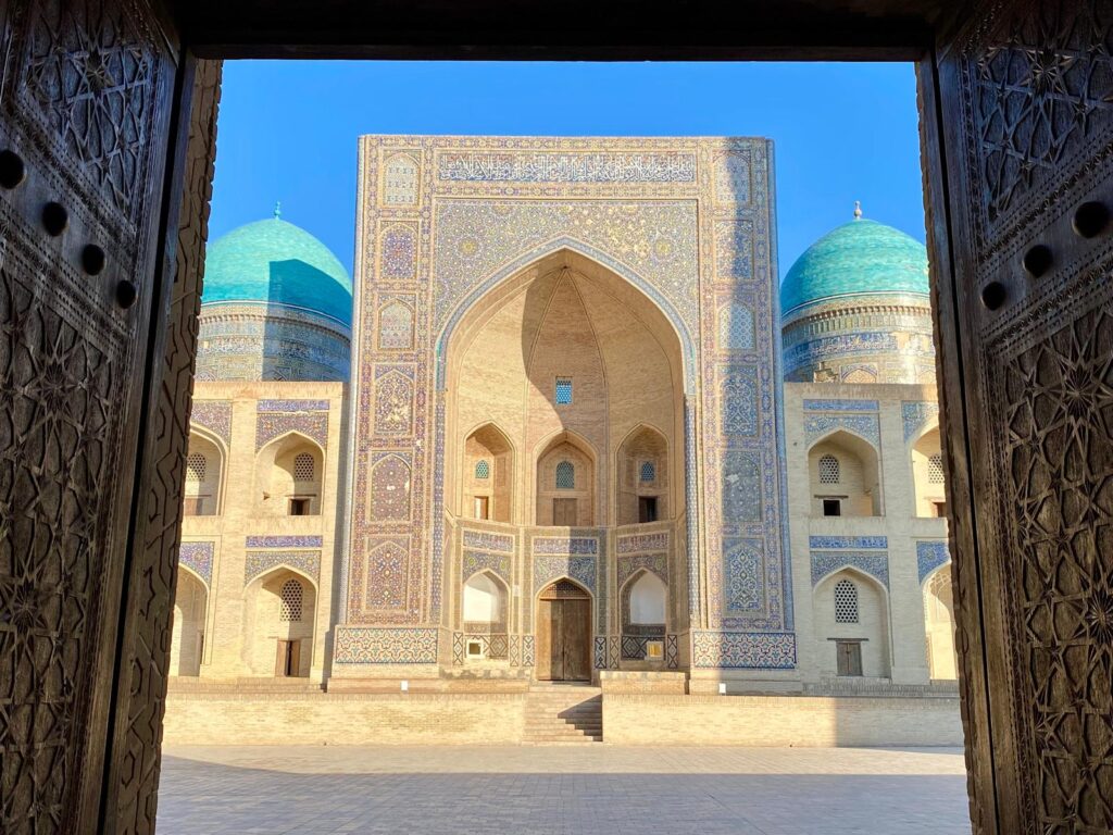 Madrasa storica con cupole turchesi vista attraverso un portale monumentale in Uzbekistan